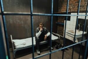 A solitary prisoner in a dimly lit cell, sitting on a bed in deep thought, evoking a sense of isolation and introspection.