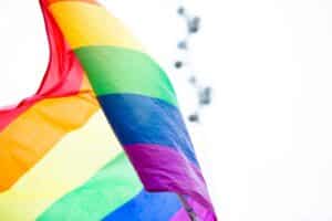A colorful rainbow pride flag waves against a bright sky, symbolizing LGBTQ+ celebration and diversity.