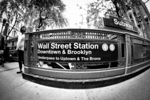 Black and white image of Wall Street subway entrance in New York City, capturing urban life.