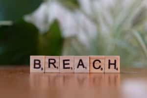 Wooden letter tiles spell 'Breach' against a blurred natural background, concept of security or violation.
