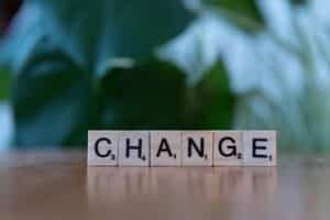 Scrabble tiles spelling 'CHANGE' on a wooden surface with a blurred green background.