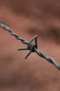 High angle detail of metal barbed wire fence against blurred background of field