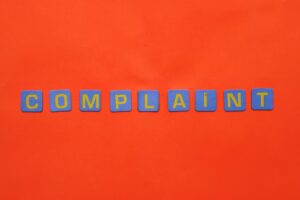 Blue letter tiles spelling 'COMPLAINT' on a vibrant red surface.