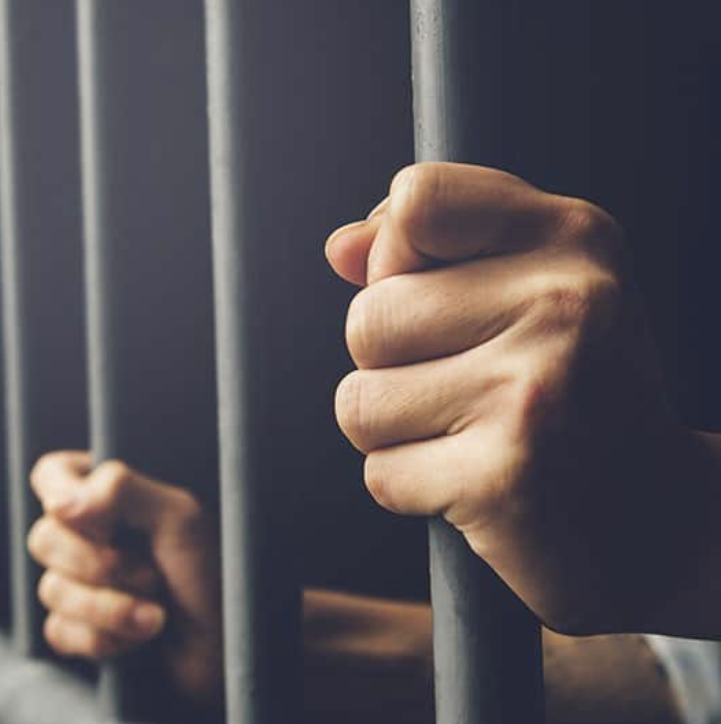A hand gripping prison bars in a darkened cell.