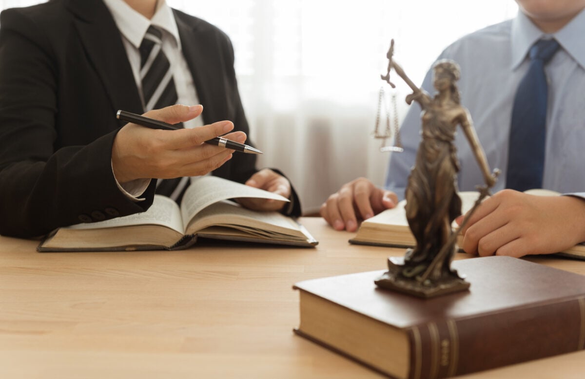 Two people at a desk with law books and a small statue of Lady Justice.